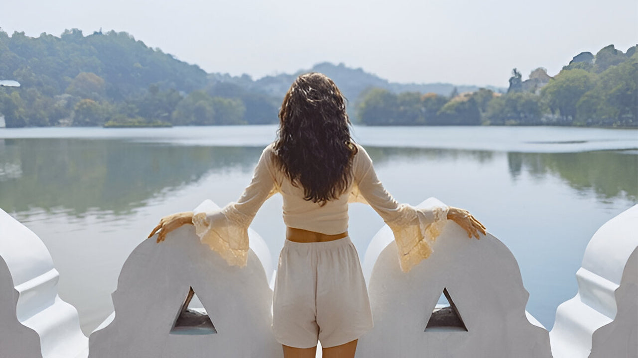 Woman standing on a decorative stone bench by a lake with trees in the background